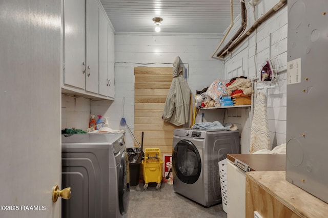 clothes washing area with wood walls, cabinet space, and washing machine and dryer