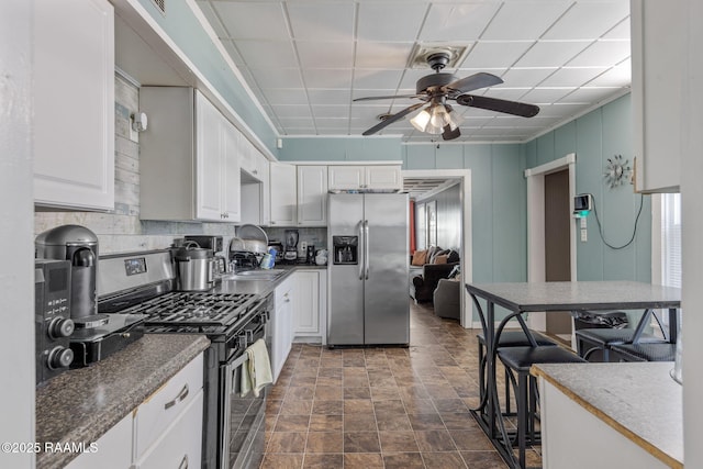 kitchen with a sink, ceiling fan, white cabinetry, stainless steel appliances, and a drop ceiling
