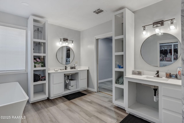bathroom featuring visible vents, baseboards, a freestanding bath, a sink, and wood finished floors