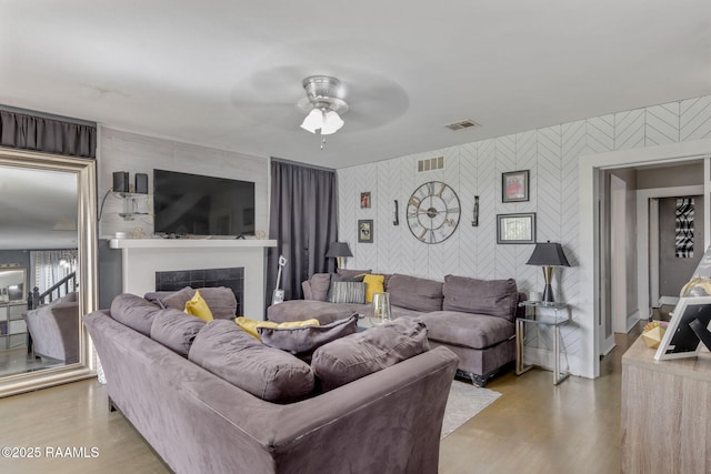 living area with ceiling fan, an accent wall, visible vents, a tile fireplace, and wallpapered walls