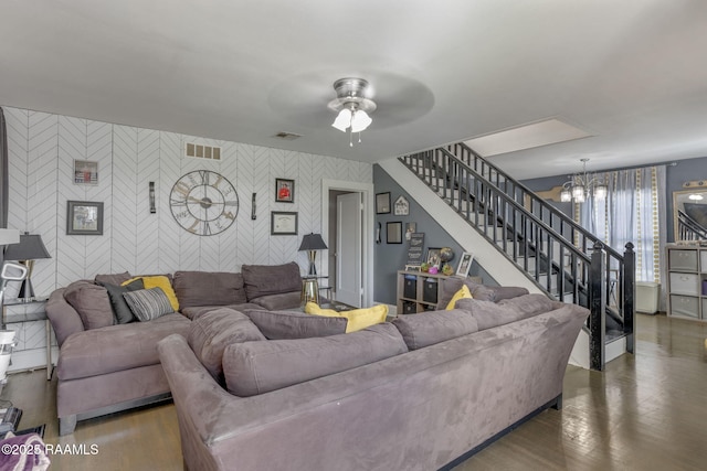 living room featuring ceiling fan with notable chandelier, an accent wall, visible vents, stairs, and wallpapered walls
