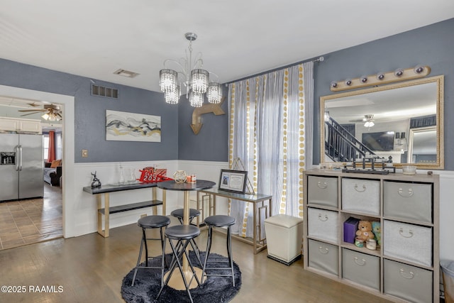 dining room with visible vents, a wainscoted wall, wood finished floors, and ceiling fan with notable chandelier