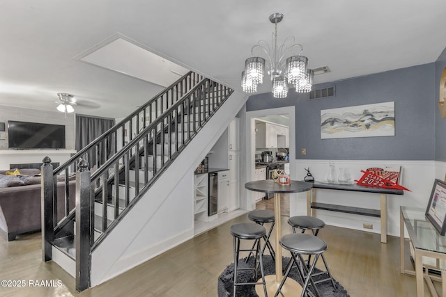 interior space with wainscoting, visible vents, beverage cooler, ceiling fan with notable chandelier, and wood finished floors