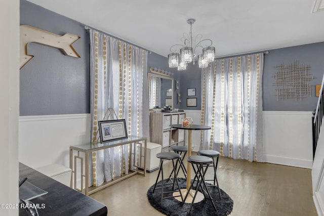 dining space with an inviting chandelier, wainscoting, wood finished floors, and a healthy amount of sunlight