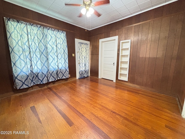 unfurnished room featuring wooden walls, a ceiling fan, and wood finished floors