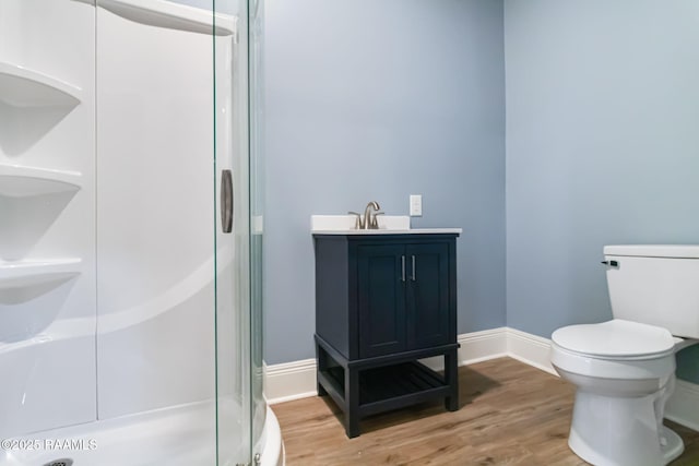 bathroom with toilet, a sink, wood finished floors, a stall shower, and baseboards