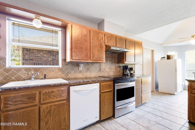 kitchen with a sink, white appliances, under cabinet range hood, vaulted ceiling, and decorative backsplash