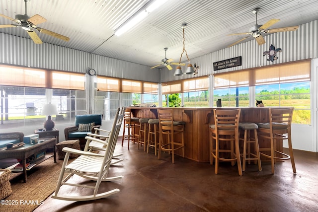 interior space with a bar, a ceiling fan, a healthy amount of sunlight, high vaulted ceiling, and finished concrete floors