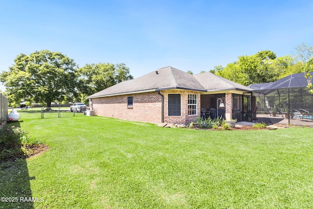 rear view of property with fence, brick siding, a lanai, and a lawn