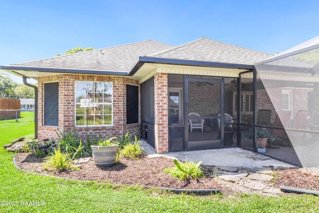 back of house with brick siding, a sunroom, and roof with shingles