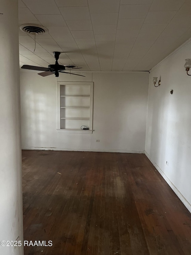 spare room featuring built in features, a ceiling fan, visible vents, baseboards, and dark wood-style floors