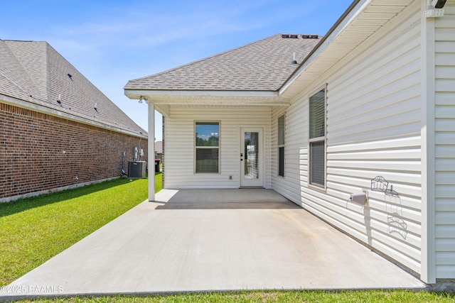 back of house with central air condition unit, roof with shingles, a yard, and a patio area