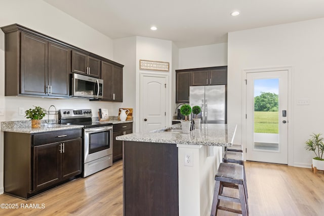 kitchen featuring a sink, light wood-type flooring, dark brown cabinetry, a kitchen bar, and stainless steel appliances
