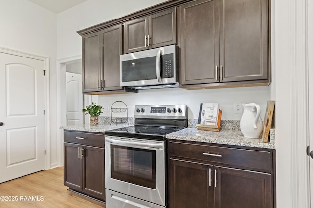 kitchen with dark brown cabinetry, light wood-type flooring, light stone counters, and appliances with stainless steel finishes