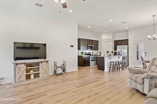 living area featuring visible vents, light wood-style floors, and ceiling fan with notable chandelier