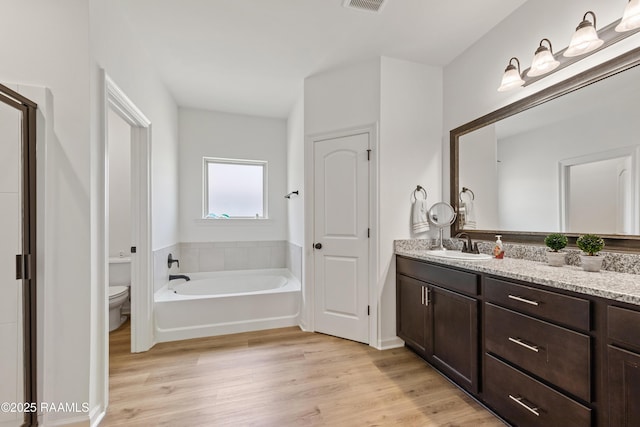 bathroom featuring vanity, a bath, toilet, and wood finished floors