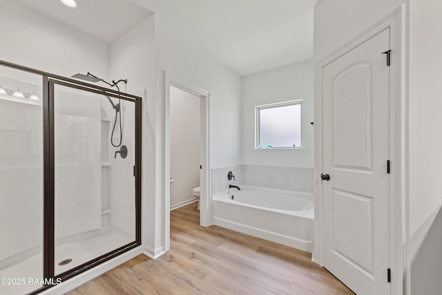 bathroom featuring a bath, baseboards, toilet, a shower stall, and wood finished floors