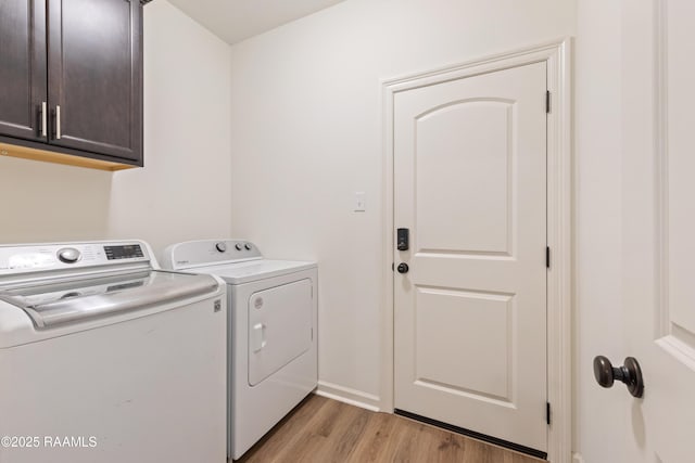 clothes washing area with light wood finished floors, baseboards, washing machine and clothes dryer, and cabinet space
