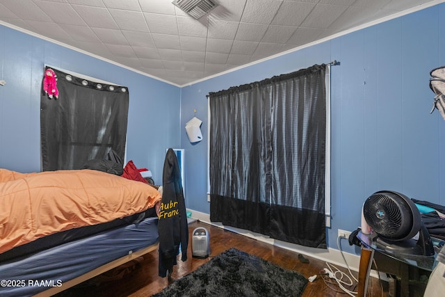 bedroom featuring wood finished floors, ornamental molding, and visible vents