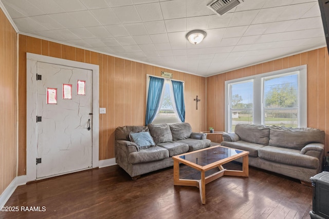 living area with wood finished floors, wood walls, ornamental molding, and visible vents