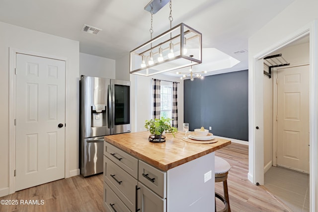 kitchen featuring visible vents, butcher block counters, a kitchen bar, light wood-type flooring, and stainless steel fridge