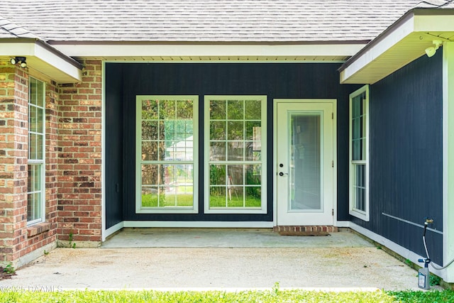 entrance to property featuring brick siding and roof with shingles