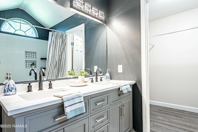 bathroom featuring double vanity, wood finished floors, vaulted ceiling, a shower with curtain, and a sink