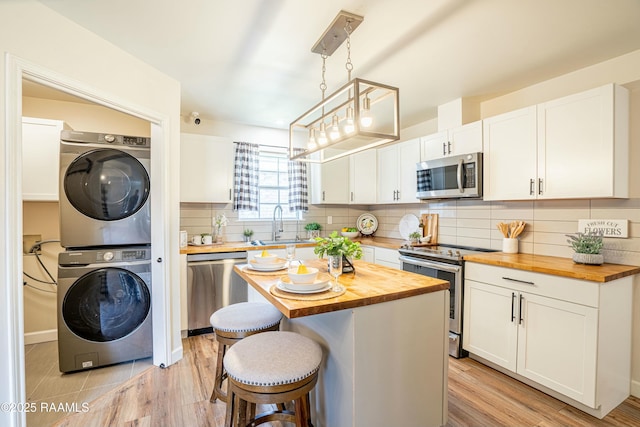 kitchen featuring stacked washer / drying machine, white cabinets, a kitchen breakfast bar, stainless steel appliances, and butcher block counters
