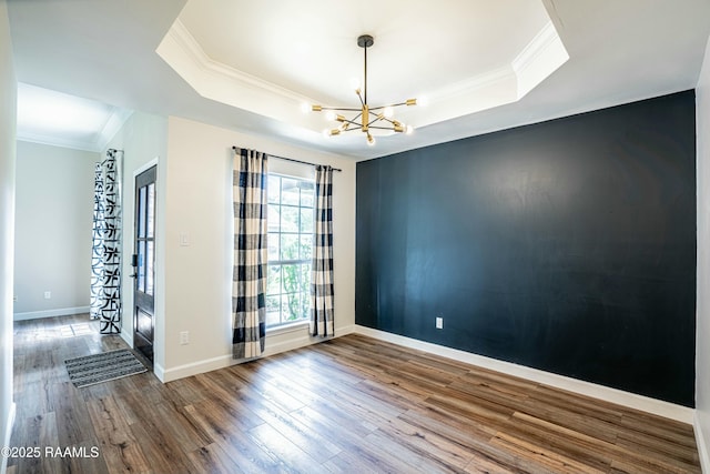 unfurnished room with a tray ceiling, baseboards, a notable chandelier, wood finished floors, and crown molding