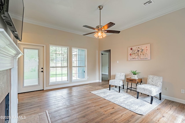 sitting room with wood finished floors, visible vents, crown molding, a fireplace, and ceiling fan