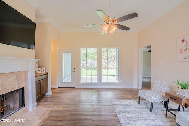 interior space featuring ceiling fan, baseboards, a tile fireplace, and light wood-style floors
