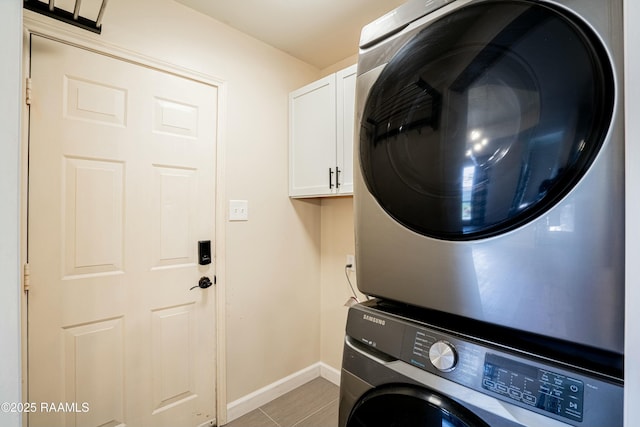 clothes washing area with stacked washer and dryer, baseboards, and cabinet space