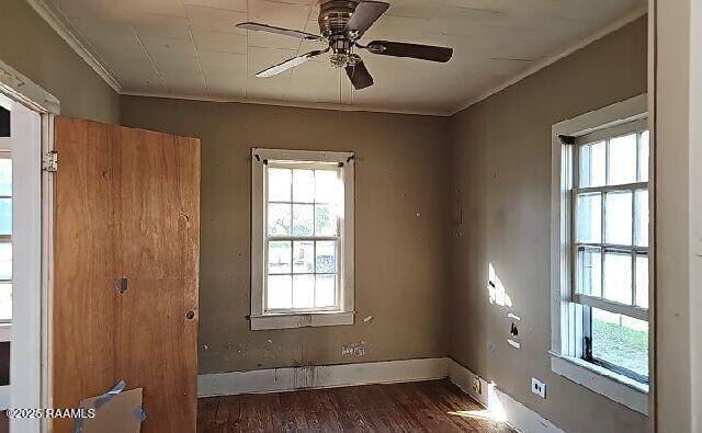 empty room featuring plenty of natural light, a ceiling fan, wood finished floors, and ornamental molding