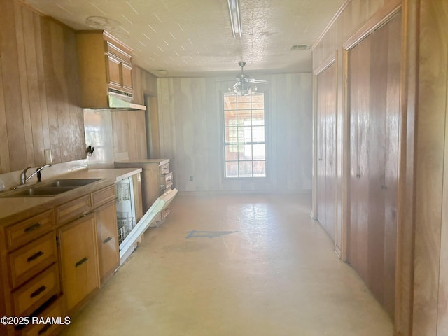 kitchen featuring finished concrete flooring, visible vents, a sink, brown cabinets, and wooden walls