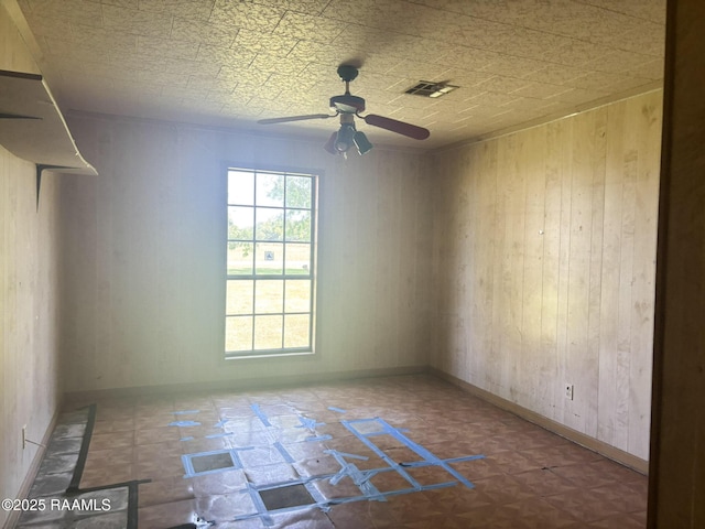 spare room with ceiling fan, baseboards, wooden walls, and visible vents