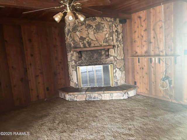 unfurnished living room featuring a stone fireplace, carpet flooring, a ceiling fan, wood walls, and wooden ceiling