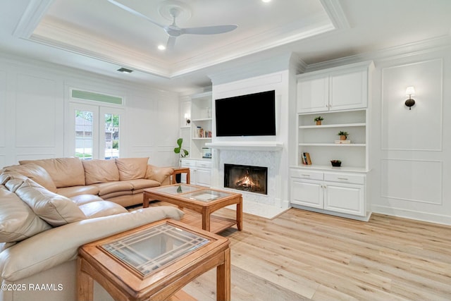 living area featuring ceiling fan, a raised ceiling, light wood-style floors, a decorative wall, and a premium fireplace