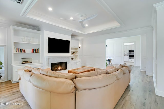 living area with ceiling fan, crown molding, a raised ceiling, light wood finished floors, and a premium fireplace