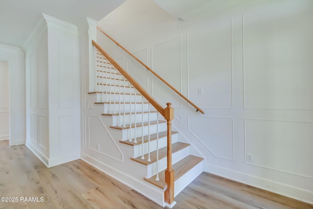 staircase with wood finished floors, crown molding, and a decorative wall