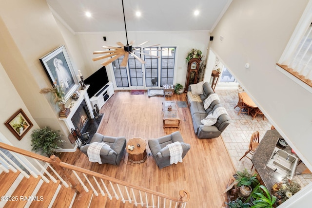 living room with wood finished floors, a glass covered fireplace, baseboards, ornamental molding, and recessed lighting