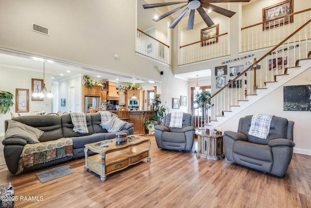 living area with stairway, crown molding, ceiling fan with notable chandelier, light wood-style floors, and visible vents