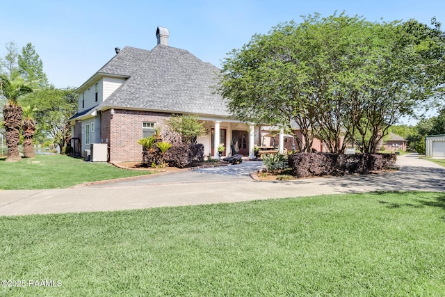 view of front facade with central air condition unit, a chimney, a shingled roof, a front yard, and brick siding