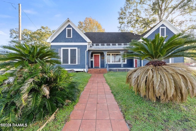 view of front of home with covered porch, a front yard, and roof with shingles