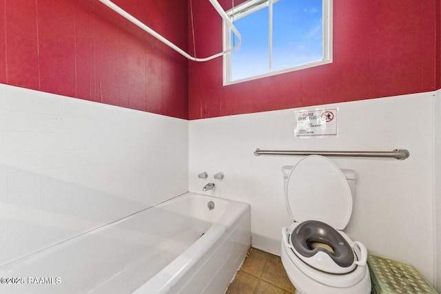 bathroom with a bath, wainscoting, tile patterned flooring, and toilet