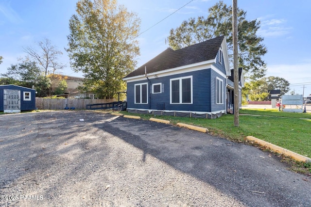 view of side of property featuring a storage shed, an outbuilding, roof with shingles, fence, and a lawn