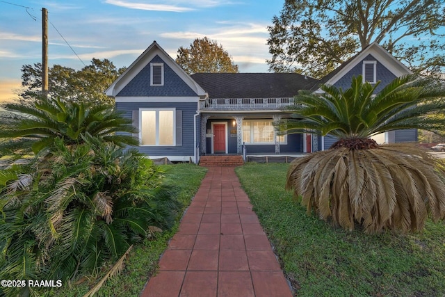 view of front facade with roof with shingles, a front yard, and covered porch