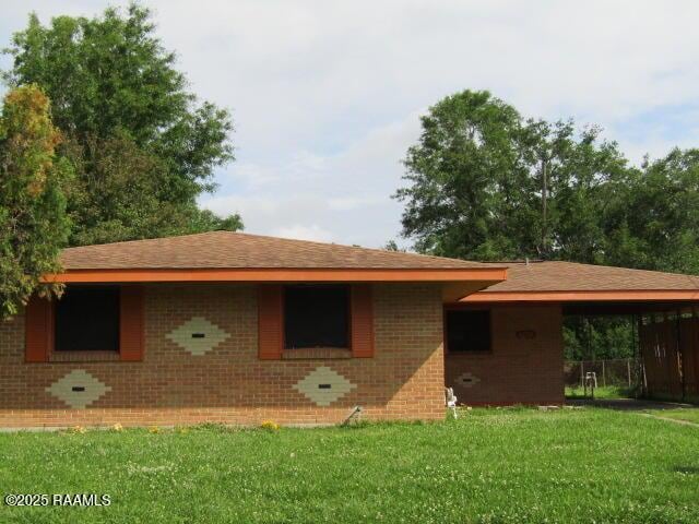 back of property with a carport, a lawn, and brick siding