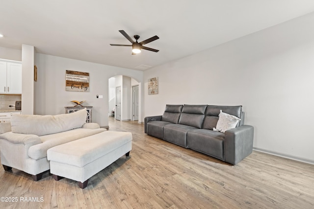 living room with ceiling fan, arched walkways, light wood finished floors, baseboards, and recessed lighting