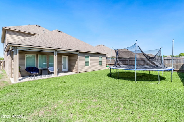 rear view of property with a fenced backyard, a trampoline, a patio area, a shingled roof, and a yard