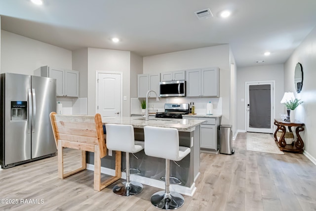 kitchen with visible vents, appliances with stainless steel finishes, gray cabinets, and a kitchen breakfast bar